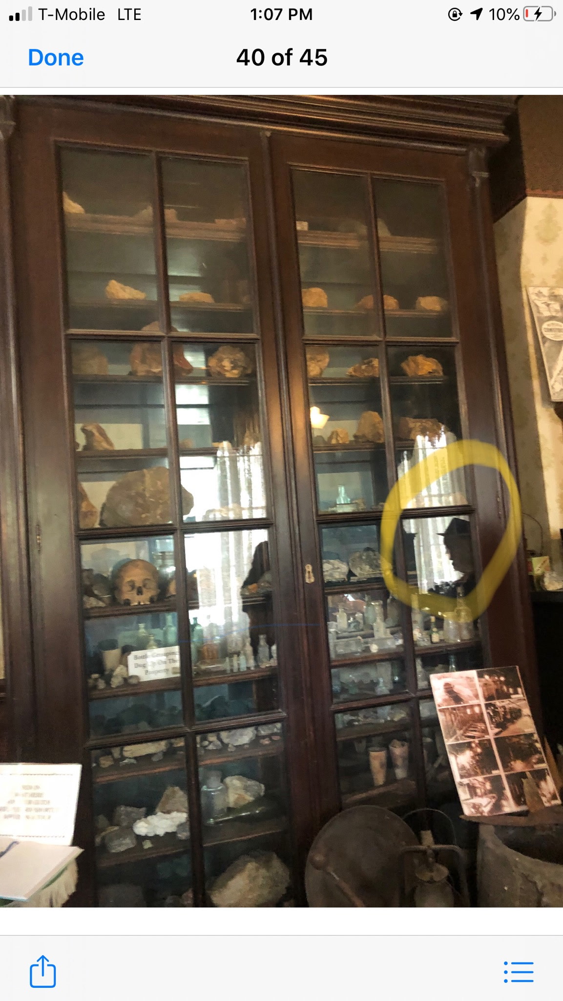 Visitor photograph of antique display cabinet with yellow circle highlighting a dark profile-like reflection